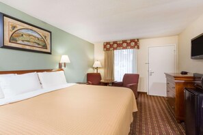 Habitación de hotel con cama, escritorio, silla, televisor y un cuadro en la pared.