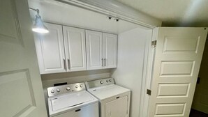 A laundry room with a washer and dryer, cabinets above, and a door to the right. - Stylish 2 Bedroom Apartment Downtown High Point (High Point)