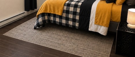 A bedroom with a bed, a rug, a nightstand, and a wall-mounted picture.