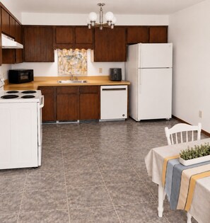 A kitchen with wooden cabinets, a white refrigerator, a microwave, a stove, and a sink. - Value, Function & Free Breakfast (Sumas)
