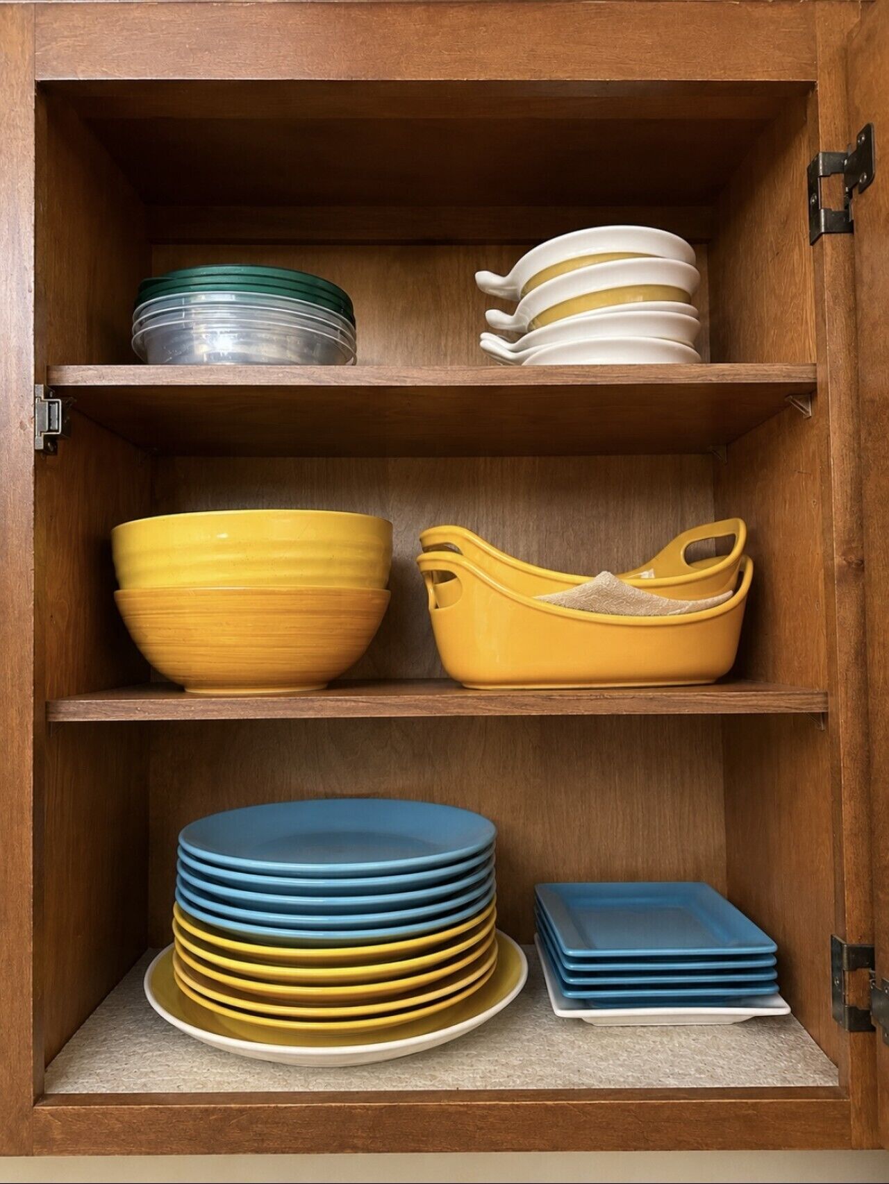 A wooden cabinet with three shelves containing various kitchenware.