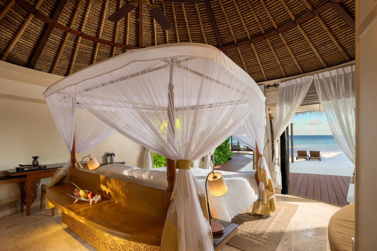 A bedroom with a canopy bed, a wooden desk, and a view of the beach.