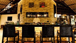 Un bar interno con una parete in pietra, un soffitto in legno e un bancone bar con sedie.