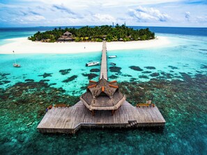 An overwater bungalows with a wooden deck and thatched roof, connected to a white sandy beach by a wooden walkway. - Banyan Tree Maldives Vabbinfaru (Vabbinfaru)