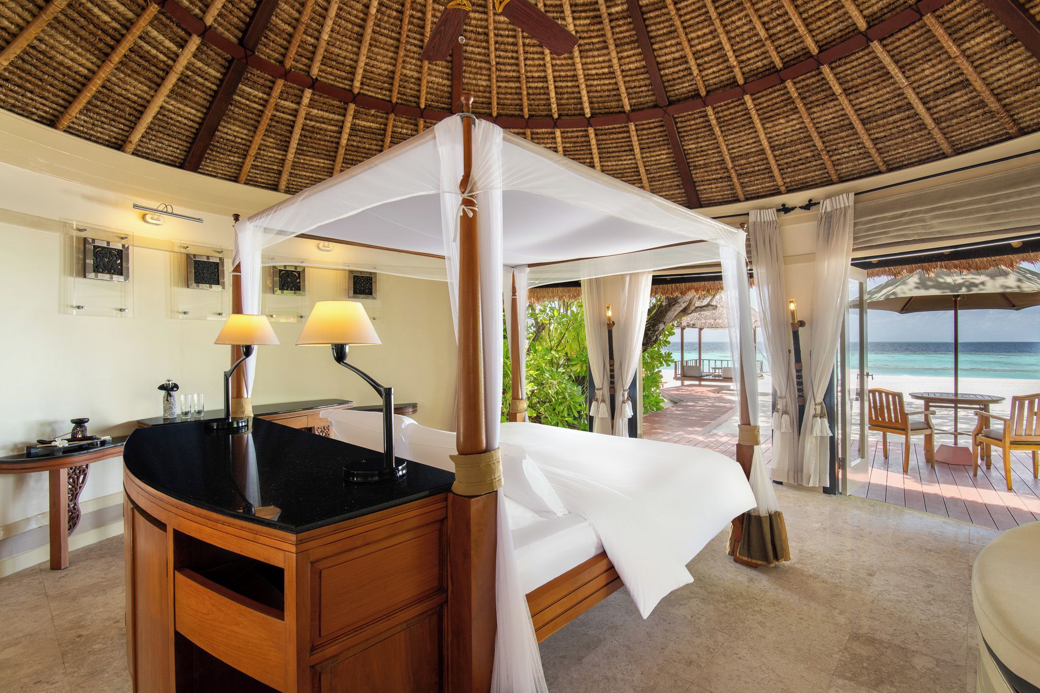 Una habitación con cama bajo un dosel, un escritorio con lámpara y vista a la playa.