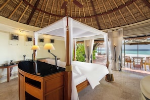 A room with a bed under a canopy, a desk with a lamp, and a view of the beach. - Banyan Tree Maldives Vabbinfaru (Vabbinfaru)