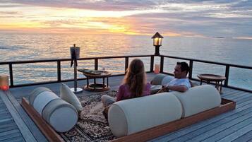 A couple relaxing on a deck with a view of the ocean at sunset.