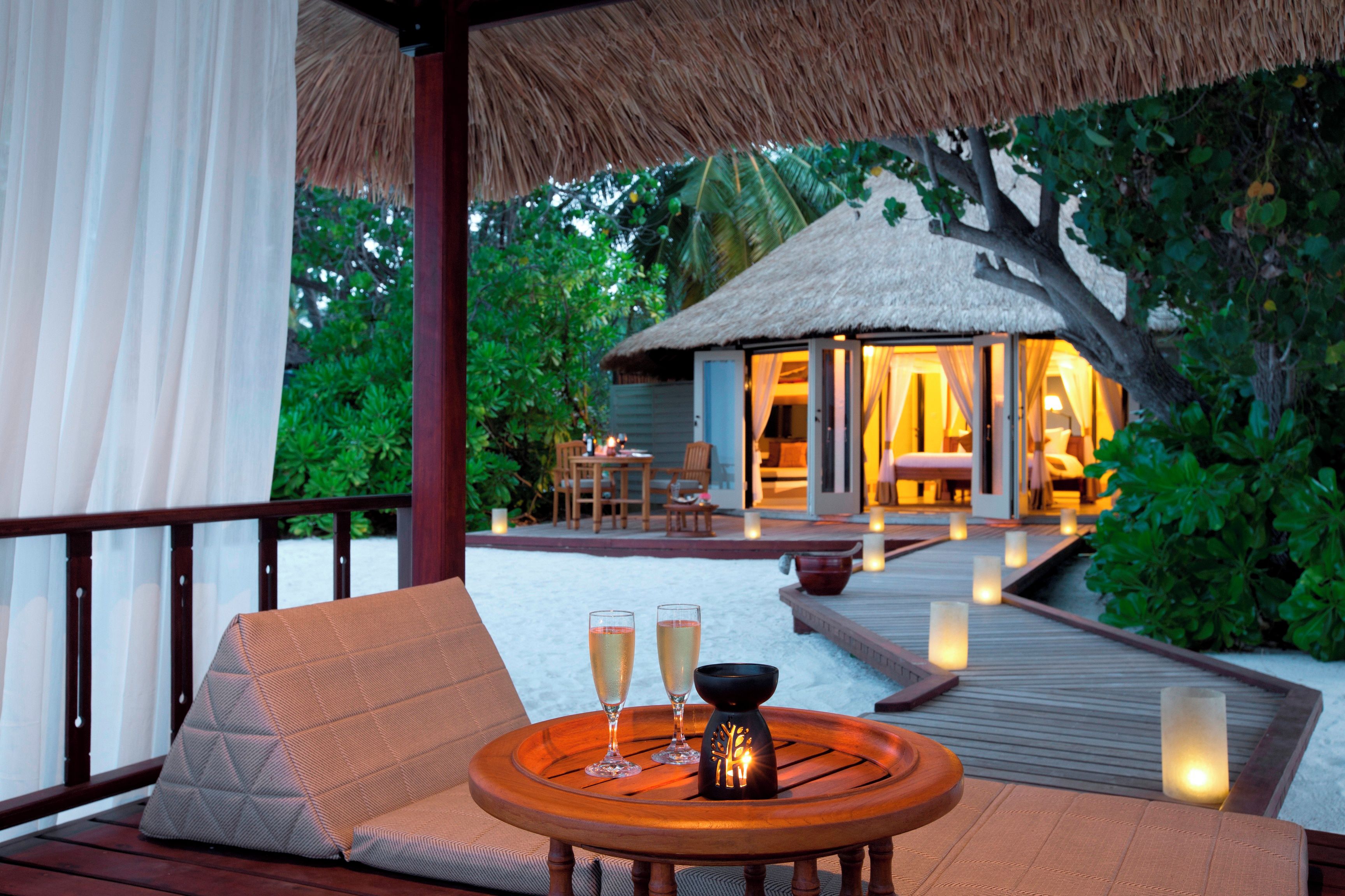 A wooden deck with a cushioned seating area, two glasses of champagne, and a lit candle on a table.