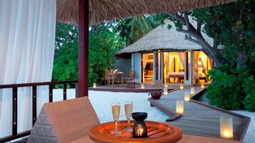 A wooden deck with a cushioned seating area, two glasses of champagne, and a lit candle on a table.