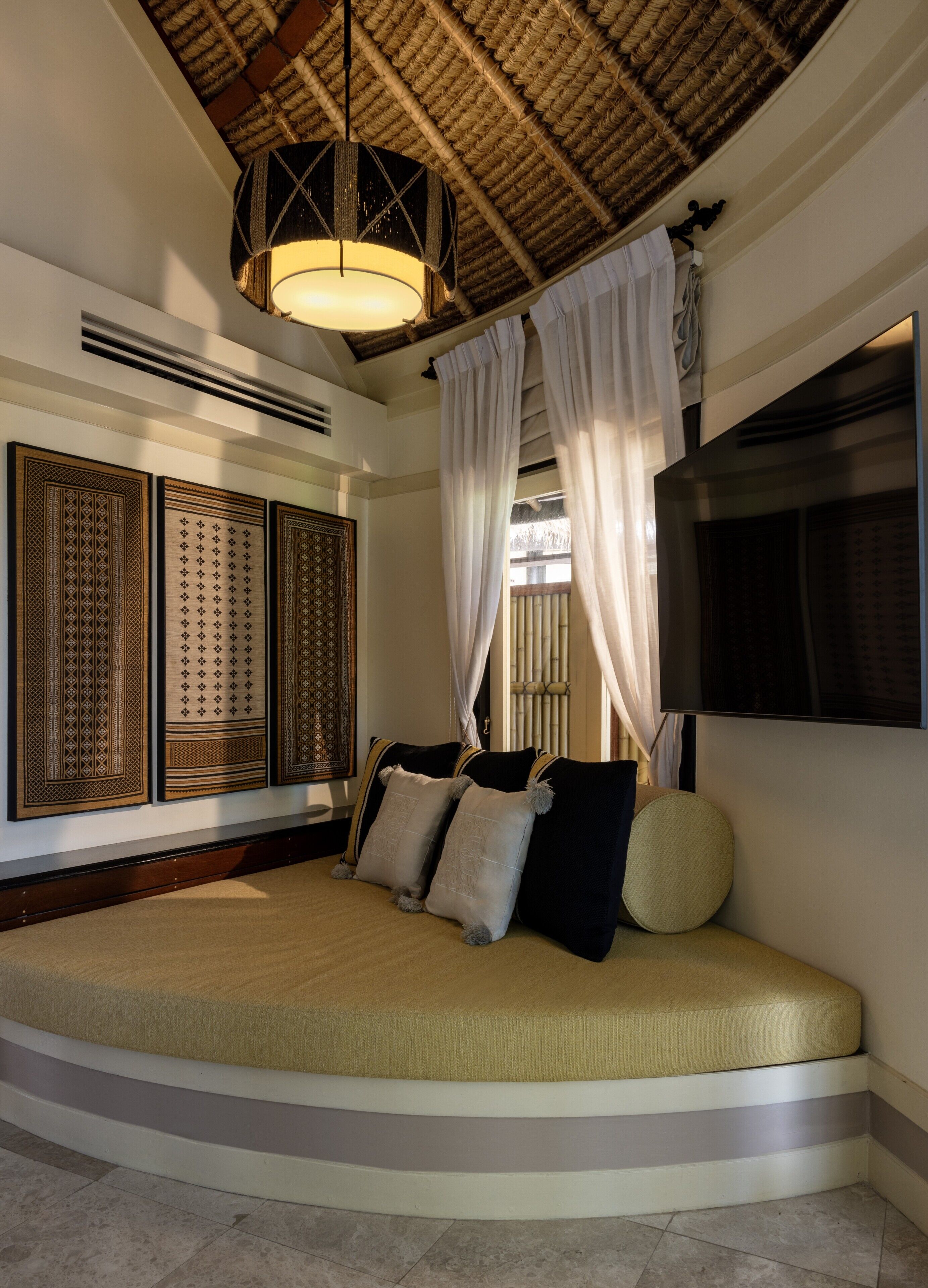 A room with a curved sofa bed, a hanging light fixture, and a large woven ceiling.