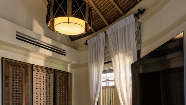 Una stanza con un divano letto curvo, una lampada a sospensione e un grande soffitto in vimini.