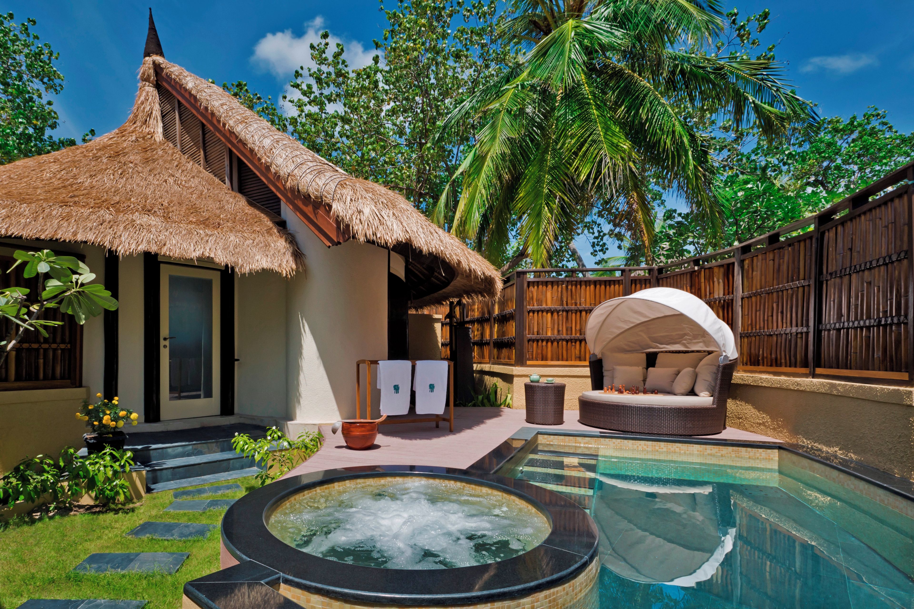 A thatched-roof house with a hot tub, a lounge area, and a pool.