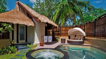 A thatched-roof house with a hot tub, a lounge area, and a pool.