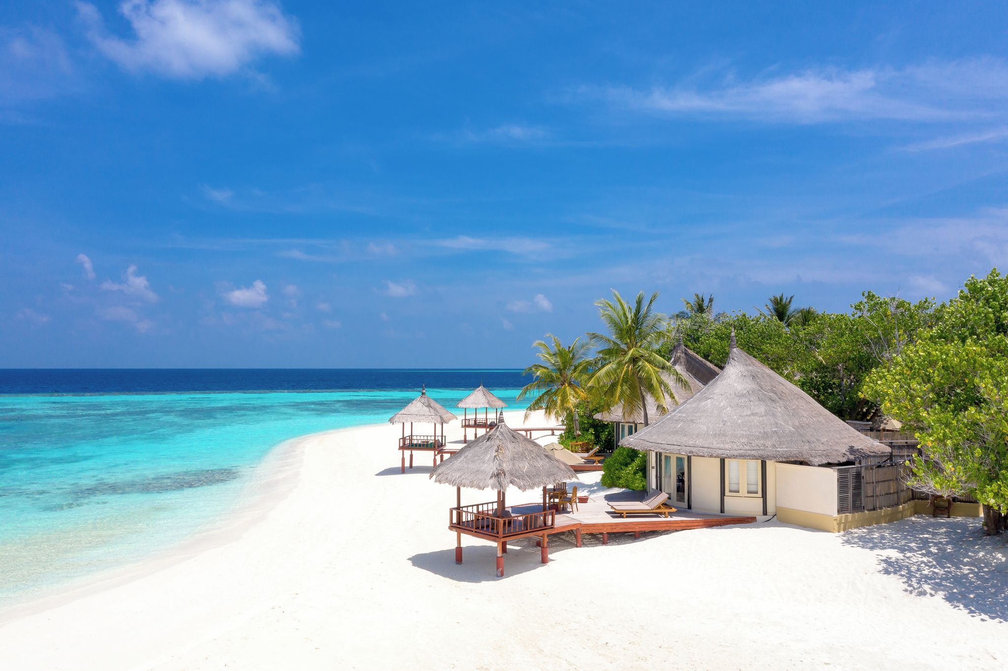A beach resort with thatched-roof huts, a white sandy beach, and clear turquoise water.