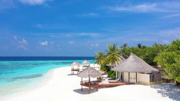 A beach resort with thatched-roof huts, a white sandy beach, and clear turquoise water.