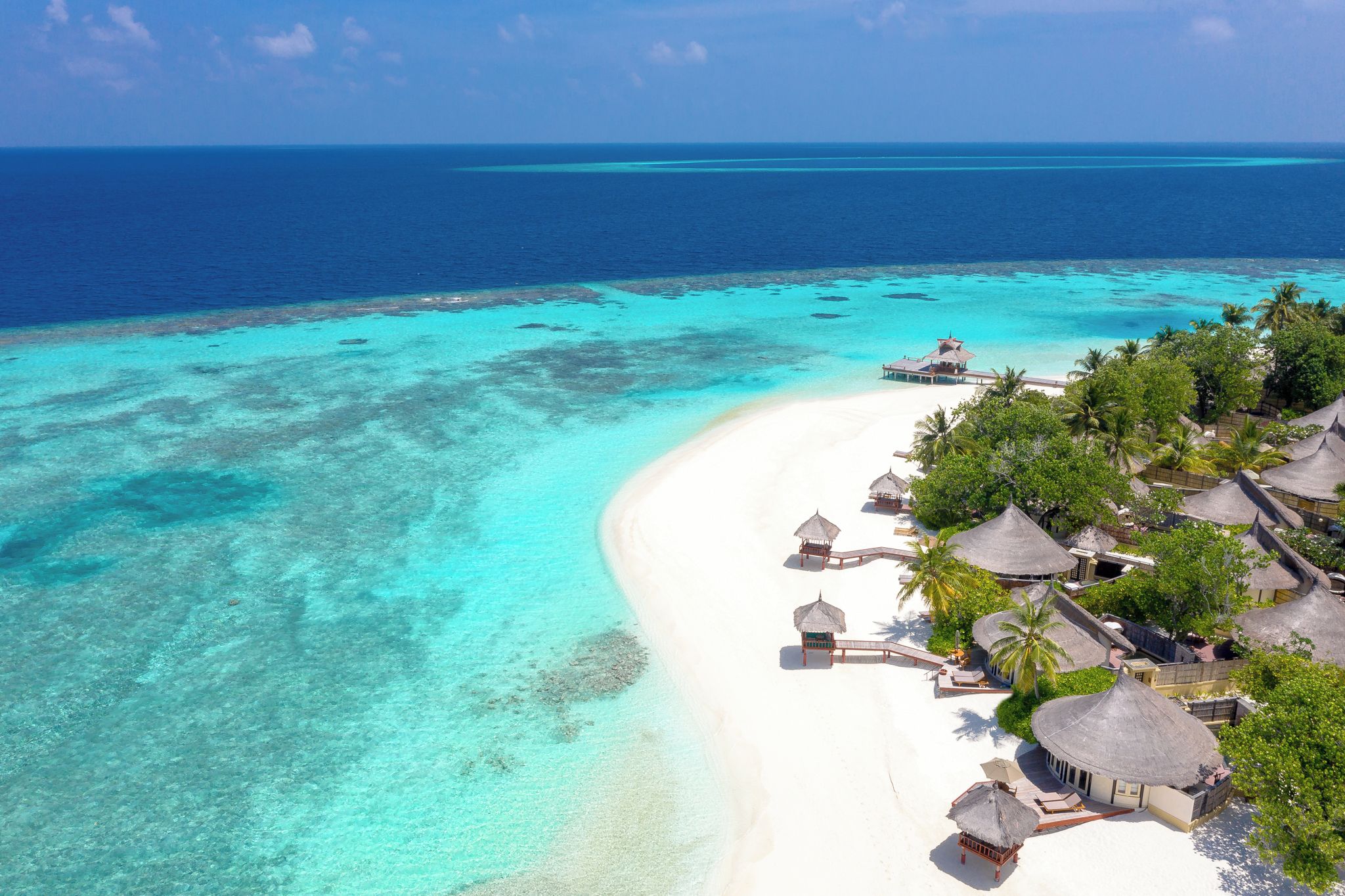 An aerial view of a beach resort with overwater bungalows, clear turquoise waters, and a white sandy beach.