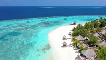 An aerial view of a beach resort with overwater bungalows, clear turquoise waters, and a white sandy beach.