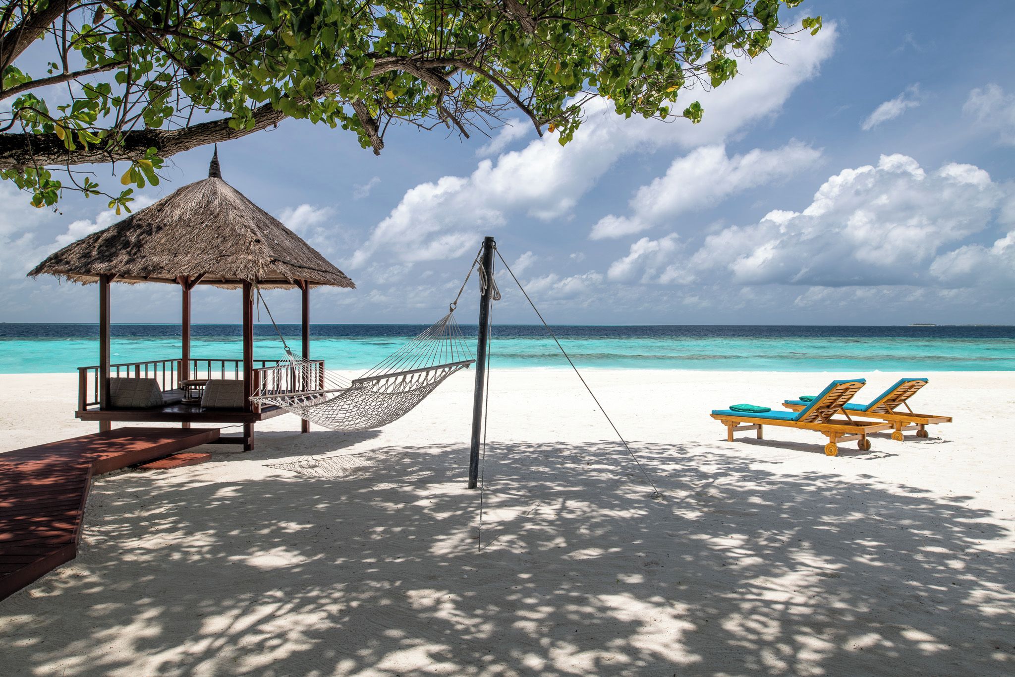 A beach with a thatched hut, a hammock, and sun loungers.
