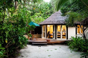 A thatched-roof structure with a wooden deck, surrounded by lush greenery.