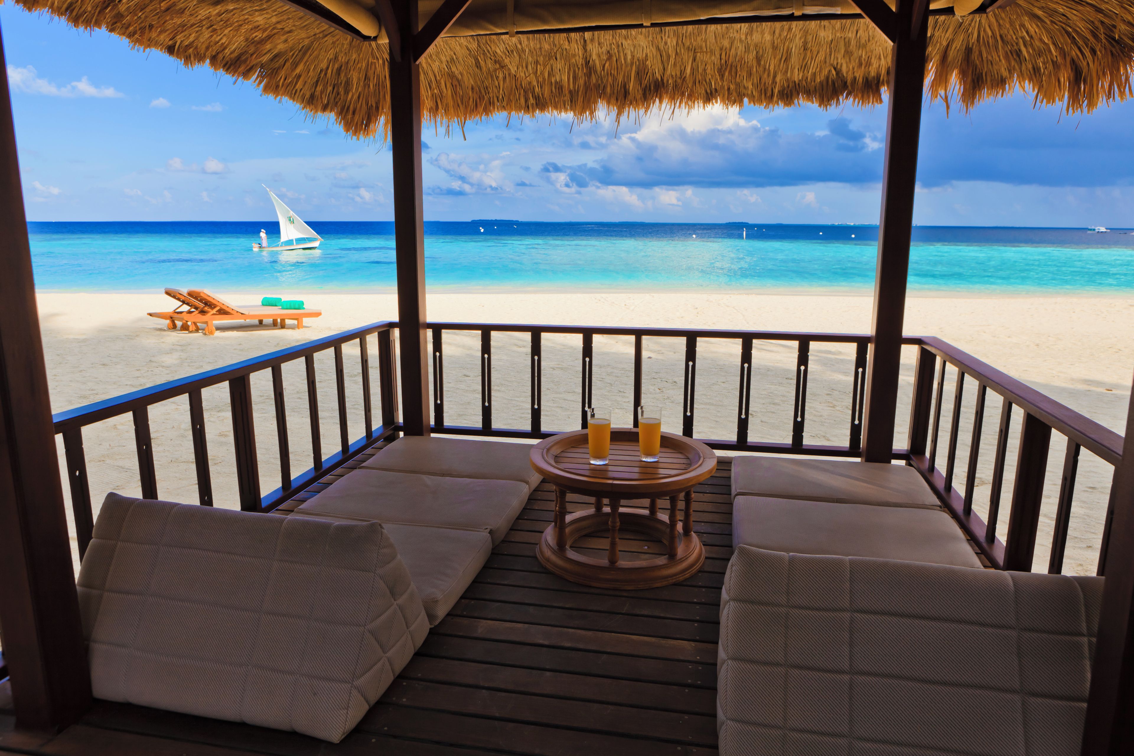 A beach view from a covered deck with lounge chairs and a table.