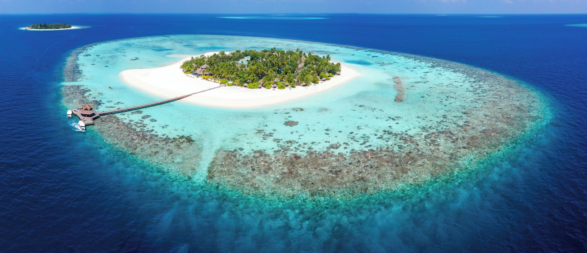 An aerial view of a tropical island with a white sandy beach, clear turquoise waters, and a small pier extending into the sea.