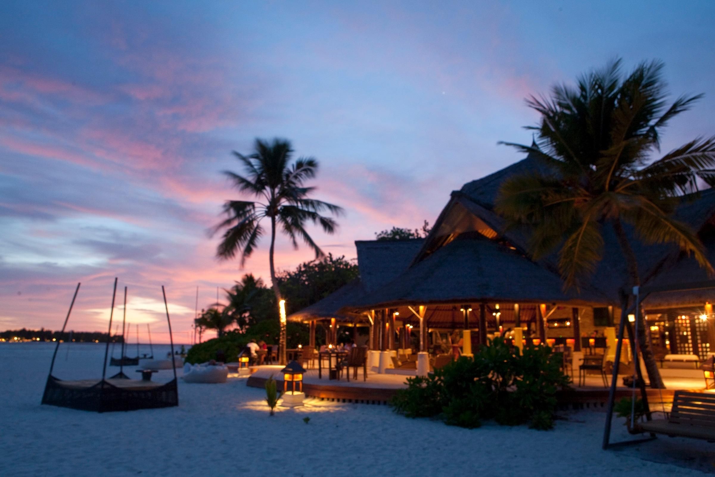 A beachfront resort with a thatched-roof building, palm trees, and a sandy beach.