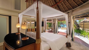 A four-poster canopy bed with a black countertop and a lamp, a television, and a view of the beach and palm trees. - Banyan Tree Maldives Vabbinfaru (Vabbinfaru)