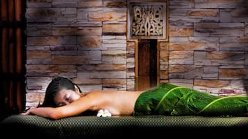 A person lying on a massage table in a room with a stone wall and a wooden panel.