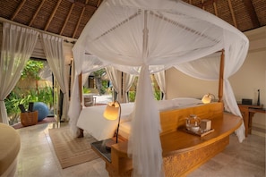 A room with a bed under a canopy, a bedside table with a lamp, and a view of the outdoors. - Banyan Tree Maldives Vabbinfaru (Vabbinfaru)