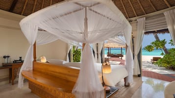 Un dormitorio con cama con dosel, un banco de madera, una mesita de noche y vista a la playa.