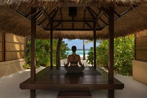 A person meditating on a wooden platform with a thatched roof, overlooking a beach. - Banyan Tree Maldives Vabbinfaru (Vabbinfaru)