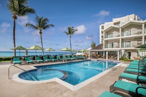 A pool area with lounge chairs and umbrellas, a building with balconies, and palm trees.