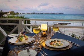 A table set for two with plates of food, two glasses of wine, and a candle on a balcony overlooking the sea.