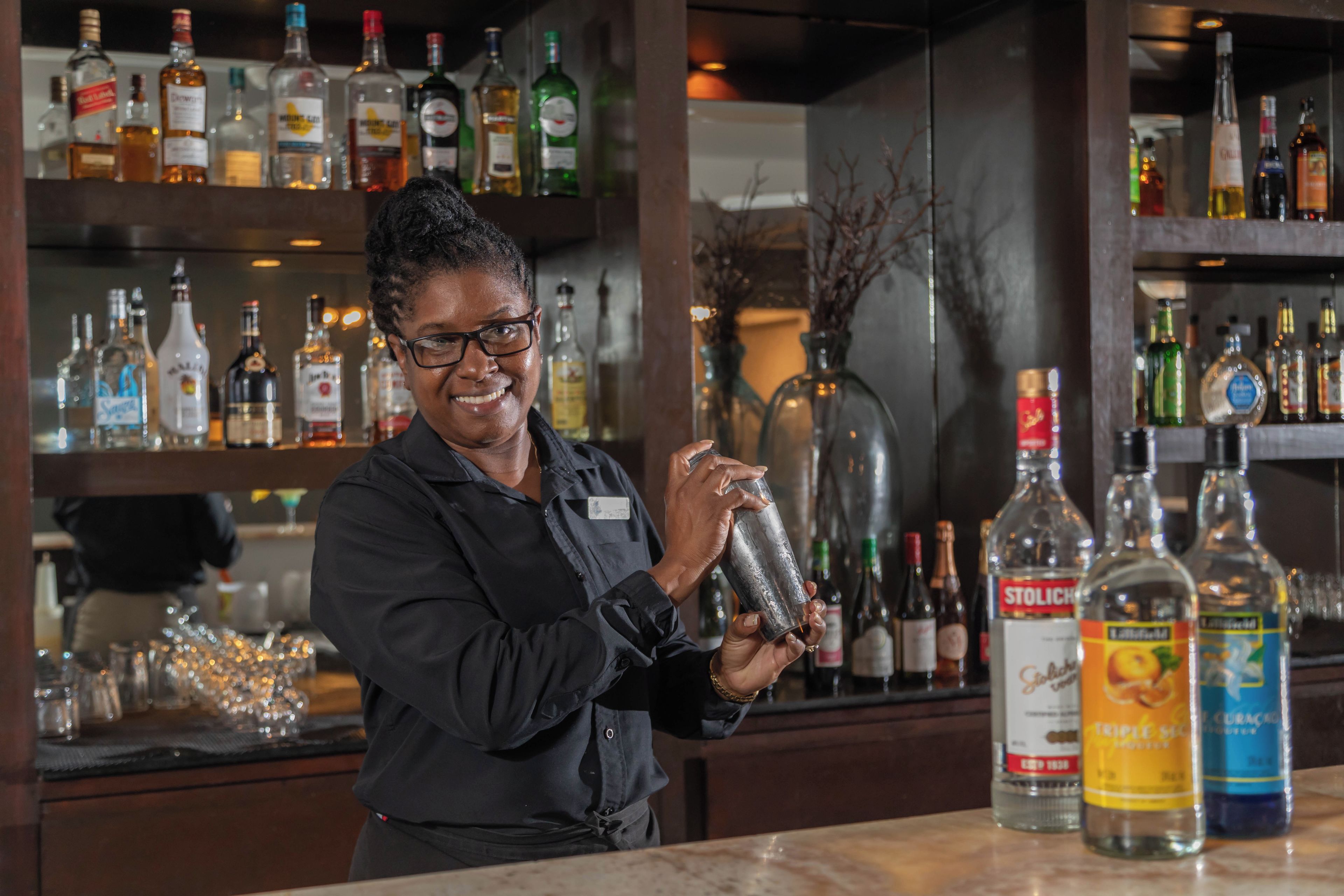 A bartender preparing a drink behind a bar with various bottles of alcohol.