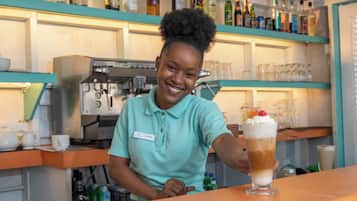 A person in a teal shirt behind a bar counter with a beverage in front of them.