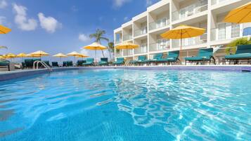 A swimming pool with lounge chairs and umbrellas, surrounded by a building with multiple balconies.