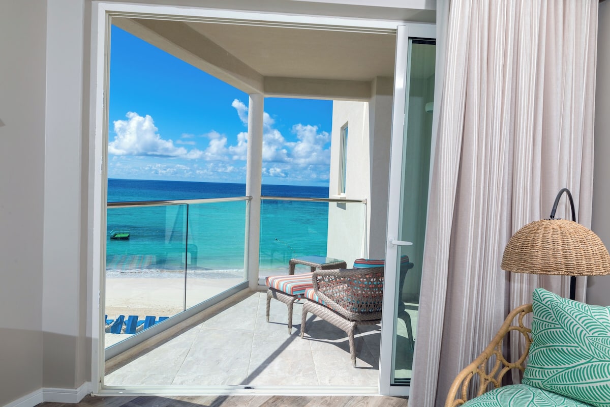 A balcony with a view of the ocean, wicker furniture, and a hanging lamp.