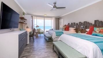 A hotel room with a TV, two beds, a desk, and a view of the ocean.