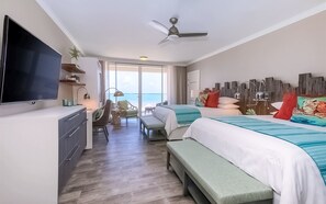 A hotel room with a TV, two beds, a desk, and a view of the ocean.