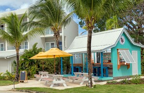 A beachside hotel with outdoor seating, palm trees, and a turquoise building. - Sea Breeze Beach House All Inclusive by Ocean Htls (CHRIST CHURCH)
