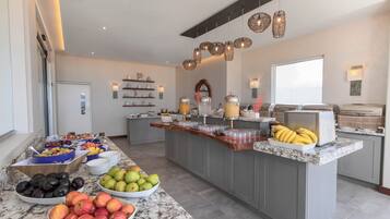 A modern kitchen with a marble countertop, a fruit bowl, and a buffet area with various food items.