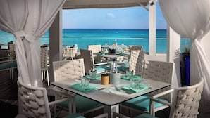 An outdoor dining area with tables and chairs, a view of the ocean, and a covered structure. - Sea Breeze Beach House All Inclusive by Ocean Htls (CHRIST CHURCH)