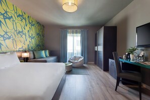 Een moderne hotelkamer met een groot bed, een bank, een relax fauteuil, een bureau met stoel, een televisie en een raam met gordijnen.
