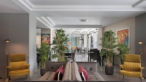 Ein modernes Wohnzimmer mit einer Couch, zwei Sesseln und einem Essbereich mit Tisch und Stühlen. Üppige Zimmerpflanzen und Kunstwerke zieren die Wände.