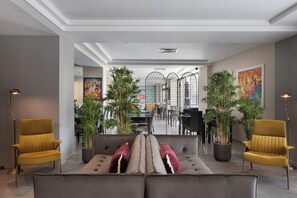 Een moderne woonkamer met een bank, twee fauteuils en een eethoek met een tafel en stoelen. Er staan potplanten en er hangt kunst aan de muren.