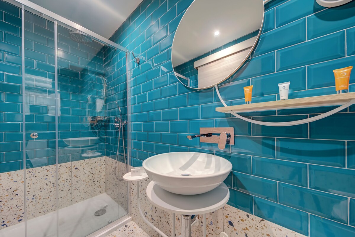 Een badkamer met een douche met glazen wand, een wit wastafelmeubel en een muur betegeld met blauwe tegels.
