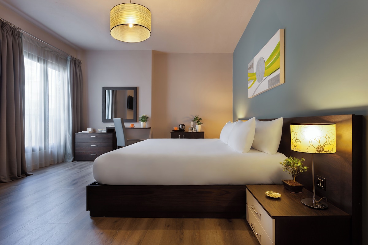 Een moderne hotelkamer met een groot bed, nachtkastje, lamp en een kleine kamerplant.