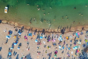 Vista aérea de una playa con gente, sombrillas y un bote.