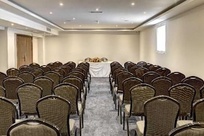 Un salón de conferencias con filas de sillas orientadas hacia una mesa cubierta con mantel blanco y un arreglo floral.