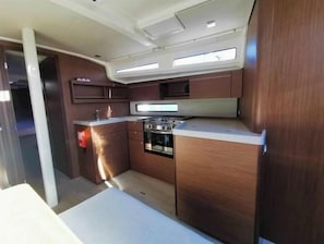 A compact kitchen with wooden cabinets, a stove, and a countertop. - Oceanis 40.1 - 4D cab - DORY (Pomer)